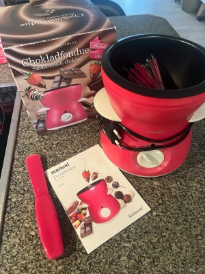 Ceriserosa chokladfondue från Rubicson - Elektrisk chokladfondue i ceriserosa plast och metall från Rubicson. Medföljer flera fonduegafflar, manual och originalkartong. Perfekt för att smälta choklad och doppa frukt eller godis. Enkel att använda med vred på framsidan för temperaturkontroll. Endast använd ett fåtal gånger, som ny! 