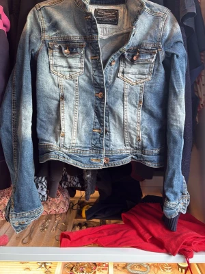 Blå klassisk jeansjacka - Snygg blå jeansjacka med slitna detaljer och kopparfärgade knappar. Två bröstfickor med lock och knapp men även 2 st framfickor, samt markerade sömmar för en klassisk look. Jackan har en något kortare passform och är perfekt för dig som gillar en tidlös stil.