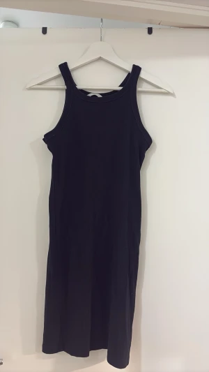 Svart ribbad klänning  - Säljer en svart ribbad klänning med tight passform och ärmlös design. Klänningen har en enkel och stilren look med rundad halsringning och är gjord i ett stretchigt material som sitter snyggt på kroppen.