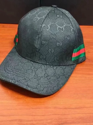 Svart Gucci keps med monogram - Säljer en svart keps från Gucci med diskret GG-monogram över hela tyget. Kepsen har böjd skärm och klassiska gröna och röda ränder på sidorna. Tillverkad i ett slitstarkt tyg som ger en exklusiv känsla och passar perfekt till streetwear-stilen.