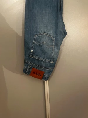 Blå slim fit jeans från Replay - Snygga blå slim fit jeans från Replay med klassisk femficksdesign och läderpatch bak i midjan. Jeansen har en lätt tvättad look och raka ben. Perfekta för en trendig och avslappnad stil.
