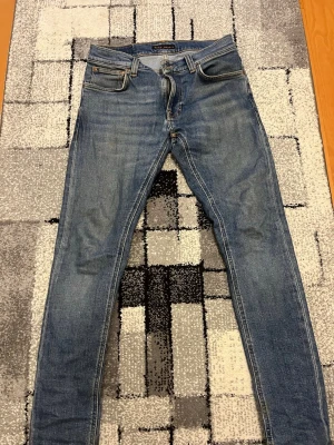 Blå tight terrys! Nudies - Säljer ett par blå slim fit jeans med klassisk femficksdesign och kontrastsömmar. Jeansen har en snygg tvättad look och broderade detaljer på bakfickorna. Materialet är troligtvis bomull med lite stretch för extra komfort.