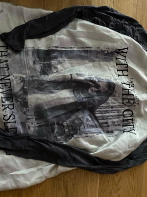 Svartvit långärmad t-shirt True Spirit - Cool långärmad t-shirt från True Spirit i svart och vitt med ett stort tryck av en stad och texten 'I am in love with the city that never sleeps' på framsidan. Perfekt för dig som gillar streetstyle och grafiska prints.