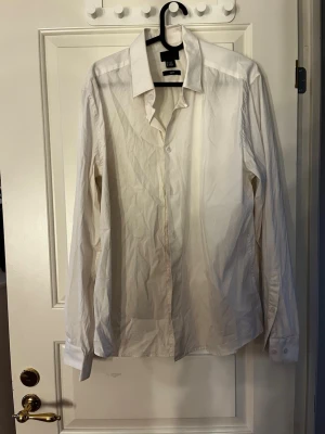 Vit slim fit skjorta från H&M - Klassisk vit skjorta från H&M i slim fit-modell. Skjortan har lång ärm, knappar framtill och en stilren krage. Tillverkad i mjuk bomull som känns skön mot huden. Perfekt för dig som gillar en clean och enkel look.