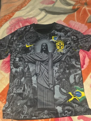 Svart Brasilien fotbollströja Nike - Unik svart fotbollströja från Nike med Brasilien-emblem och gult Nike-märke. Tröjan har ett detaljerat tryck med Kristusstatyn, brasilianska symboler och flagga. Tillverkad i lätt och andningsbart material, perfekt för träning eller match.