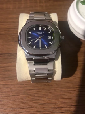 Klocka  - Stilren klocka med blå urtavla och datumvisning. Klockan har ett klassiskt armband i silverfärgat stål och en elegant, rundad fyrkantig boett. Perfekt för dig som gillar exklusiva accessoarer med tidlös design. Priset kan diskuteras!