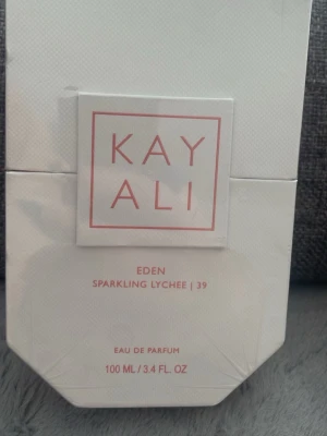 Kayali Eden Sparkling Lychee 100ml - Kayali Eden Sparkling Lychee 39 är en Eau de Parfum i en elegant vit förpackning med rosa detaljer. Doften kommer i en 100 ml flaska och har en fräsch, fruktig karaktär med inslag av litchi. Perfekt för dig som gillar unika och moderna parfymer.