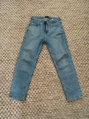 Ljusblå Lee jeans raka ben - Ljusblå jeans från Lee med raka ben och klassisk femficksdesign. Jeansen har normalhög midja, Lee-logga på bakfickan och läderpatch i midjan. Tillverkade i denim för en tidlös och avslappnad stil.
