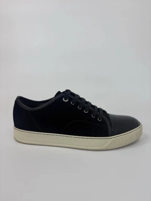 Svarta Lanvin sneakers med lackdetaljer - Stilrena svarta sneakers med snygga lackdetaljer på tån och snörning framtill. Ovandelen är i mockaliknande material och sulan är vit och platt. Perfekta för dig som gillar en clean och modern look.