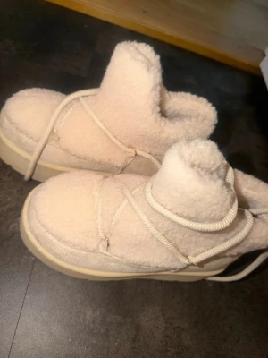 Beige fluffiga moon boots - Säljer ett par beige moon boots med fluffigt yttre och tjock sula. Skorna har snörning runt om och är perfekta för kalla dagar. De har en chunky och mysig look som sticker ut. Perfekt för dig som vill ha både stil och värme i vinter.
