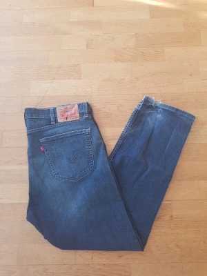 Levi's 505 - Klassiska blå jeans från Levi's med rak passform och femficksdesign. Jeansen har en tydlig röd Levi's-tag på bakfickan och ett läderpatch i midjan. Tillverkade i slitstarkt denimtyg, perfekta för en avslappnad och tidlös stil.