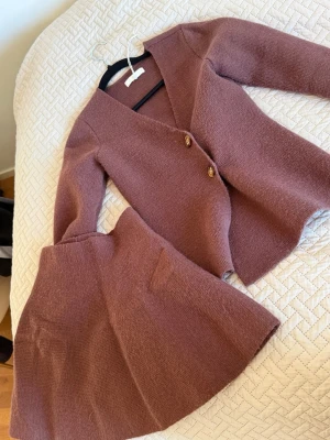 Stickat set i gammelrosa från NAKD - Säljer ett stickat set i mjuk gammelrosa färg från NAKD. Setet består av en långärmad kofta med två knappar framtill och en matchande kjol med fickor. Perfekt för dig som gillar en stilren och mysig look.