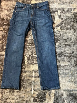 Klassiska blå raka jeans - Ett par klassiska blå jeans med rak passform och fem fickor. Jeansen har normal midja och är tillverkade i denim med synliga sömmar. Perfekta för en avslappnad och tidlös stil.
