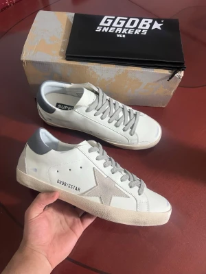 Golden Goose Superstar vita sneakers - Golden Goose Superstar sneakers i vitt läder med grå mockadetaljer och grå stjärna på sidan. Grå snörning och grå hälkappa. Klassisk låg modell med vintage-inspirerad sula och diskret branding på sidan. Perfekta för en trendig och avslappnad stil.