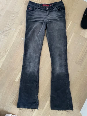 Svarta Miss Sixty bootcut jeans - Säljer ett par svarta bootcut jeans från Miss Sixty, modell Low Tommy. Jeansen har låg midja, klassisk femficksdesign och råa kanter nertill. Snyggt slitna detaljer för en cool look. Perfekta för dig som gillar vintage vibe och streetstyle.