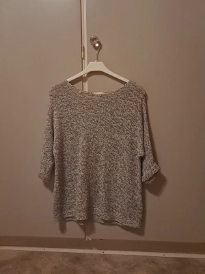Gråmelerad stickad tröja H&M - En oversized gråmelerad stickad tröja från H&M BASIC med 3/4-ärmar. Tröjan har en avslappnad passform och är perfekt för lager-på-lager. Materialet är mjukt och bekvämt, passar till många olika stilar.