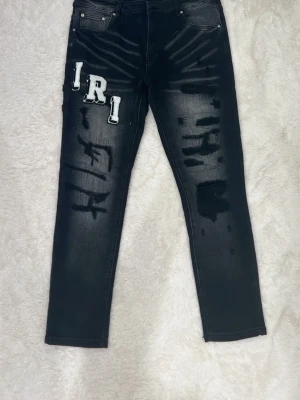 Svarta Amiri jeans med patchar och tryck - Coola svarta jeans med vita och gråa bokstavspatchar på fram- och baksida. Jeansen har skinny fit, slitna detaljer och unika tryck längs benen. Perfekta för dig som vill sticka ut med en streetstyle-look.