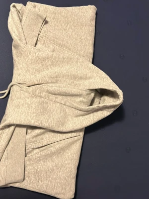 Ljusgrå hoodie med huva - Säljer en stilren ljusgrå hoodie med huva och dragsko. Hoodien har ribbade muddar vid ärmsluten och är gjord i mjukt bomullsmaterial. Perfekt för en avslappnad och bekväm look.