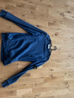 Blå sweatshirt från Stone Island - Snygg blå sweatshirt från Stone Island med klassisk rund hals och ikonisk logotyp-patch på vänster ärm. Tröjan har en avslappnad passform och är tillverkad i mjukt bomullsmaterial. Perfekt för en casual och trendig look.