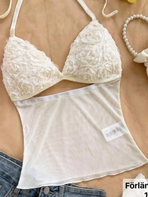 Vit mesh topp med blommiga detaljer - Snygg vit croppad topp med blommiga 3D-detaljer på bysten och transparent mesh nedtill. Aldrig använd 