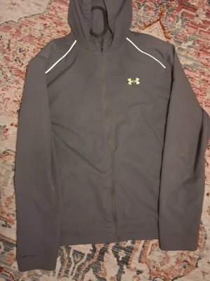 Grå Under Armour Vindjacka - Använd ett fåtal gånger, Liten hål på baksidan men syns inte från långt håll,  Storleken e M men kan även ksk psssa S,Sällsynt färg och säljs inte på butiker som JUnder Armour Osv, Skriv om ni har nåra frågor💯🫡