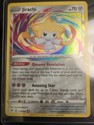 Jirachi Pokémonkort Amazing Star - Säljer ett Jirachi Pokémonkort med holografisk effekt från Sword & Shield-serien. Kortet har färgstark bakgrund, gul ram och visar Jirachi med förmågan Dreamy Revelation och attacken Amazing Star. Perfekt för samlare eller Pokémon TCG-spelare.
