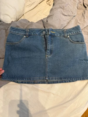 Blå jeanskjol med fickor - Snygg blå jeanskjol i klassisk modell med fem fickor, bälteshällor och dragkedja framtill. Kjolen är kort och har en rak passform, perfekt till många olika stilar. Enkel och tidlös design som är lätt att matcha. Står ingen storlek inuti men är storlek M