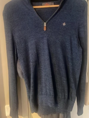 Blå halvzip-tröja från Morris - Mörkblå stickad tröja från MORRIS med halv dragkedja och liten broderad logga på bröstet. Tröjan har långa ärmar och ribbade muddar vid ärmslut och nederkant. Skick 9/10. Nypris 1699, mitt pris 800