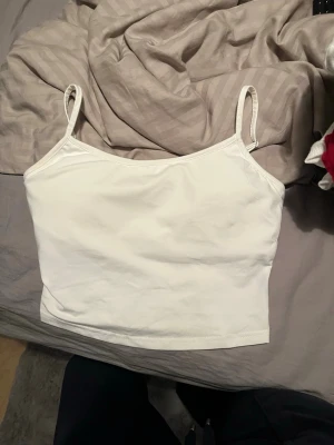 Vit enkel linnetopp med smala band - Säljer en vit linnetopp med smala axelband och rak passform. Toppen är ärmlös och har en clean, minimalistisk look som passar perfekt till jeans eller kjol. Materialet känns mjukt och stretchigt, vilket gör den bekväm att bära hela dagen. De är bh in byggd