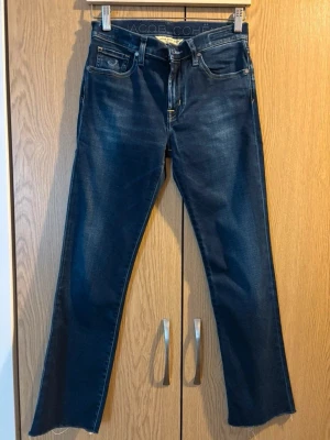 Jacob Cohën Straight Jeans - Snygga mörkblå jeans från Jacob Cohën med raka ben och klassisk femficksdesign. Jeansen har råa, avklippta benslut och subtila slitningar framtill. Tillverkade i stretchig denim Snygga straight-cut jeans från lyxmärket Jacob Cohën i mycket bra skick – knappt använda! Perfekt passform för dig som är strl 28 och vill ha ett premium-plagg i garderoben. Jacob Cohën är känt för sin exceptionella kvalitet och tidlösa design som håller år efter år. Missa inte chansen att få ett lyxmärke till ett bråk