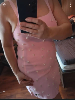Rosa kort klänning med pärlor - Säljer en söt rosa kort klänning med pärldetaljer över hela plagget. Klänningen är ärmlös och har en figurnära passform som framhäver siluetten. Perfekt för dig som vill sticka ut med en unik och trendig Look. Köpt på zara på Kreta så inget man får tag i här. 