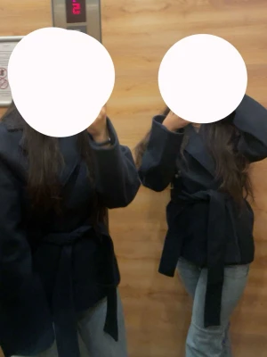 Mörkblå kappa med knytskärp - Snygg mörkblå kappa med avslappnad passform och knytskärp i midjan. Kappan har bred krage och raka ärmar, perfekt för lager på lager. Passar till jeans eller byxor för en stilren look.