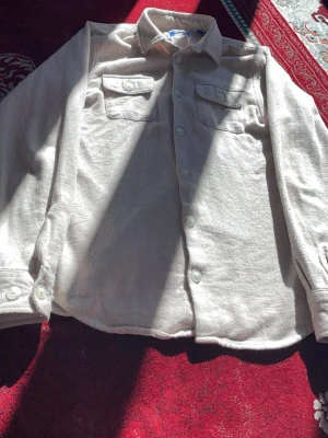 Beige overshirt från Jack and Jonas  - Stilren beige overshirt med två bröstfickor och knäppning framtill. Skjortan har klassisk krage och långa ärmar med manschettknappar. Tillverkad i mjukt, borstat tyg som ger en avslappnad look.