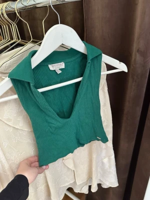 Grön ribbad croppad linnetopp - Säljer en grön ribbad linnetopp med krage och djup v-ringning. Toppen är croppad och ärmlös,