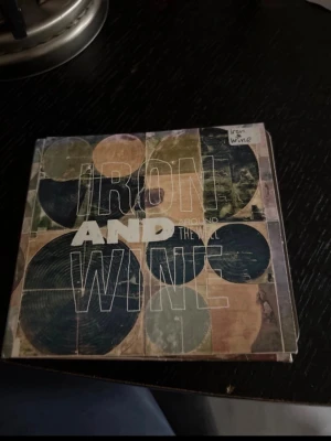 Iron & Wine Around the Well bok - Säljer en bok med titeln 'Around the Well' från Iron & Wine. Omslaget har ett konstnärligt mönster med cirklar i grönt, blått och beige. Perfekt för dig som gillar musikrelaterade  och snygg design.