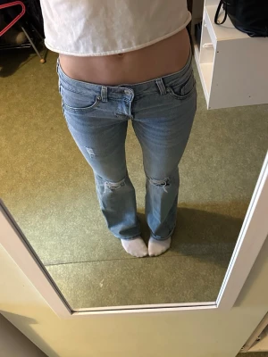 Ljusblå bootcut jeans  - Säljer ett par ljusblå bootcut jeans med slitningar och hål vid knäna. Jeansen har klassisk femficksmodell, låg midja och dragkedja med knapp. Jag är 168 cm för referens  INNERBENSLÄNGD: 78cm💕
