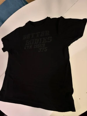 Svart Better Bodies t-shirt - Säljer en svart t-shirt från Better Bodies med tryck både fram och bak. Klassisk rund hals och korta ärmar. Perfekt för gymmet eller en avslappnad stil. Materialet känns mjukt och bekvämt mot huden.