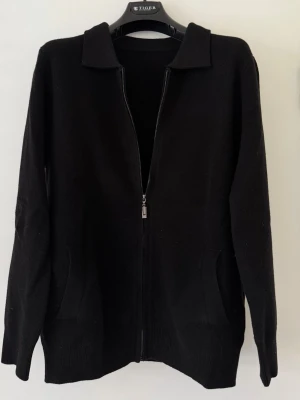  Svart zip-tröja i 100% ull - strl M - Säljer en svart zip i 100% ull, storlek M. Endast använd en gång då den tyvärr var lite för stor för mig.  Väldigt mjuk och skön kvalitet passar både till vardag och lite mer uppklätt. Dragkedja framtill och krage.  Inget märke, men känns som bra kvalitet.  Mycket fint skick, i princip som ny.
