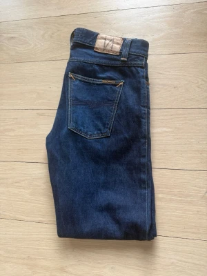 Nudie jeans  - Säljer ett par klassiska mörkblå jeans från Nudie med raka ben i Selvage modellen. Knappt använda och i väldigt fint skick.