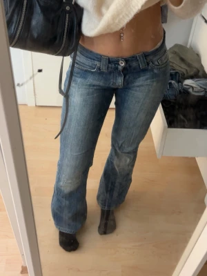 Blå bootcut jeans med låg midja - Säljer ett par blå bootcut jeans med låg midja och klassisk femficksdesign. Jeansen har en snygg tvättad look och raka ben som går ut lite nedtill. Perfekta för en avslappnad och trendig stil. Materialet är denim i bomull.