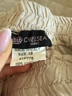 Beige linnebyxor från Chelsea - Säljer ett par ljusbeige linnebyxor från Chelsea, tillverkade i Italien. Byxorna är i 100% linne och har resår i midjan för en skön och avslappnad passform. Perfekta för en chill och stilren look. 