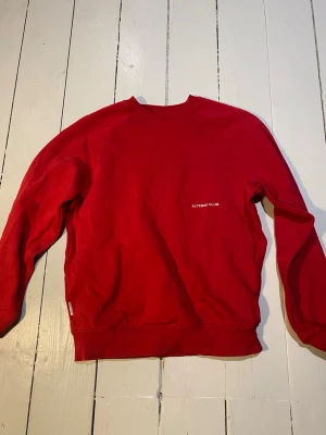 Röd sweatshirt från Yoke XS - Röd crewneck sweatshirt från Yoke med liten vit text 'ALTERED CLUB' på bröstet. Tröjan har rund hals, ribbade muddar vid ärmslut och nederkant samt en relaxed passform. Perfekt för en avslappnad och stilren look.