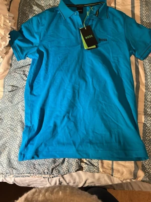 Blå pikétröja från BOSS - Snygg blå pikétröja från BOSS med klassisk krage och knappar framtill. Tröjan har korta ärmar och diskret BOSS-logga på bröstet. 