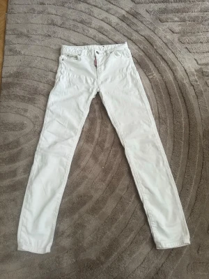 Vita jeans från DSquared2 - Säljer ett par vita skinny jeans från DSquared2 med klassisk femficksmodell och läderpatch bak i midjan. Jeansen har smal passform och är tillverkade i ett stretchigt material för extra komfort. Perfekta för dig som vill ha en clean och stilren look.