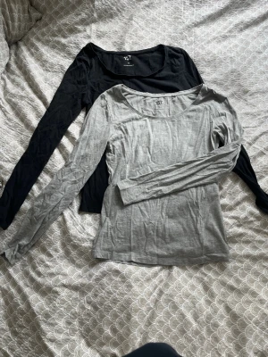 2-pack långärmade tröjor från 157 - Två basic långärmade tröjor från 157, en i svart och en i ljusgrått. Båda har rund halsringning och är tillverkade i ett mjukt, tunt material som känns skönt mot huden. Perfekta att ha som lager eller till jeans för en enkel look. Gråa tröjan är i S och den svarta i XS