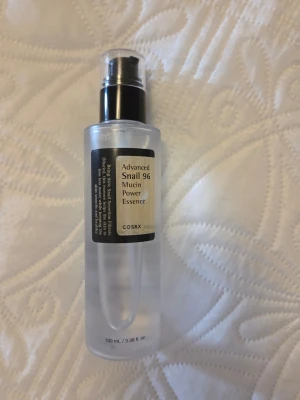 COSRX Advanced Snail 96 Essence - En genomskinlig toner i plastflaska med pump från COSRX. Advanced Snail 96 Mucin Power Essence innehåller snigelsekretfiltrat och är känd för att återfukta och stärka huden. Flaskan rymmer 100 ml och har en stilren, minimalistisk design. Endast testad en gång.