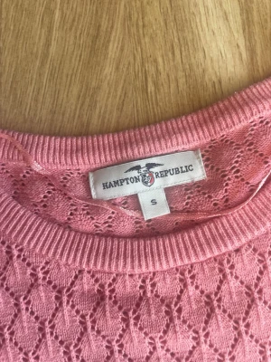 Rosa stickad topp Hampton Republic - Söt rosa stickad topp från Hampton Republic med korta ärmar och rund hals. Tröjan har ett fint hålmönster över hela plagget och ribbade kanter vid hals, ärmslut och nederkant. Har använt 1 gång så den är som ny🤗