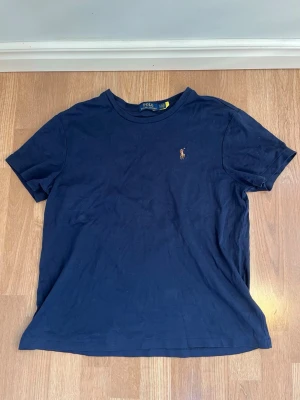 Mörkblå t-shirt från Polo Ralph Lauren - Klassisk mörkblå t-shirt från Polo Ralph Lauren med den ikoniska broderade polospelaren på bröstet. Riktigt snygg och sitter skönt. Perfekt nu till sommaren och våren. Tveka inte på att höra av dig ifall du undrar något!✨