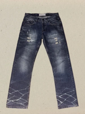 Blå slitna jeans med mönster - Säljer ett par blå jeans med slitningar och hål på låren. Jeansen har raka ben. Perfekta för dig som gillar en streetwear-look och vill sticka ut lite extra.