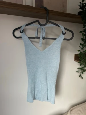 Ljusblå ribbad linnetopp BIKBOK - Supersöt ljusblå ribbad linnetopp med knyt i nacken och v-ringad hals. Toppen är ärmlös och har en mjuk, stretchig passform som sitter snyggt på kroppen. Perfekt för varma dagar och enkel att styla med jeans eller kjol.